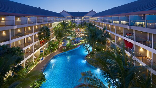 Un hôtel doté d’une piscine centrale, entourée d’une végétation luxuriante, et de plusieurs étages avec des balcons.