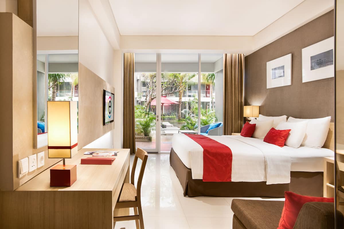 A hotel room with a bed, desk, chair, and a view of the outdoor area.