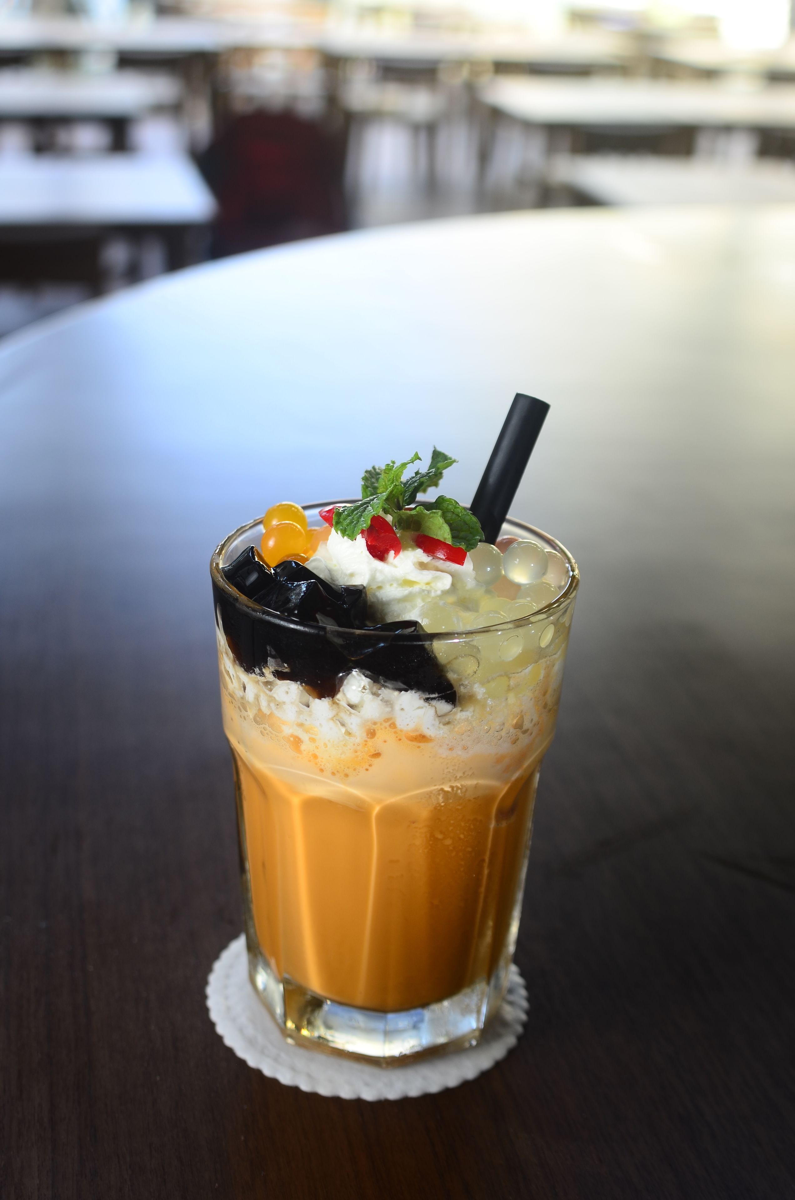 A glass of iced coffee with whipped cream, fruit, and a straw on a table.