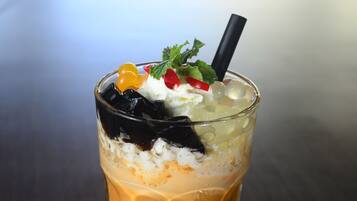 A glass of iced coffee with whipped cream, fruit, and a straw on a table.