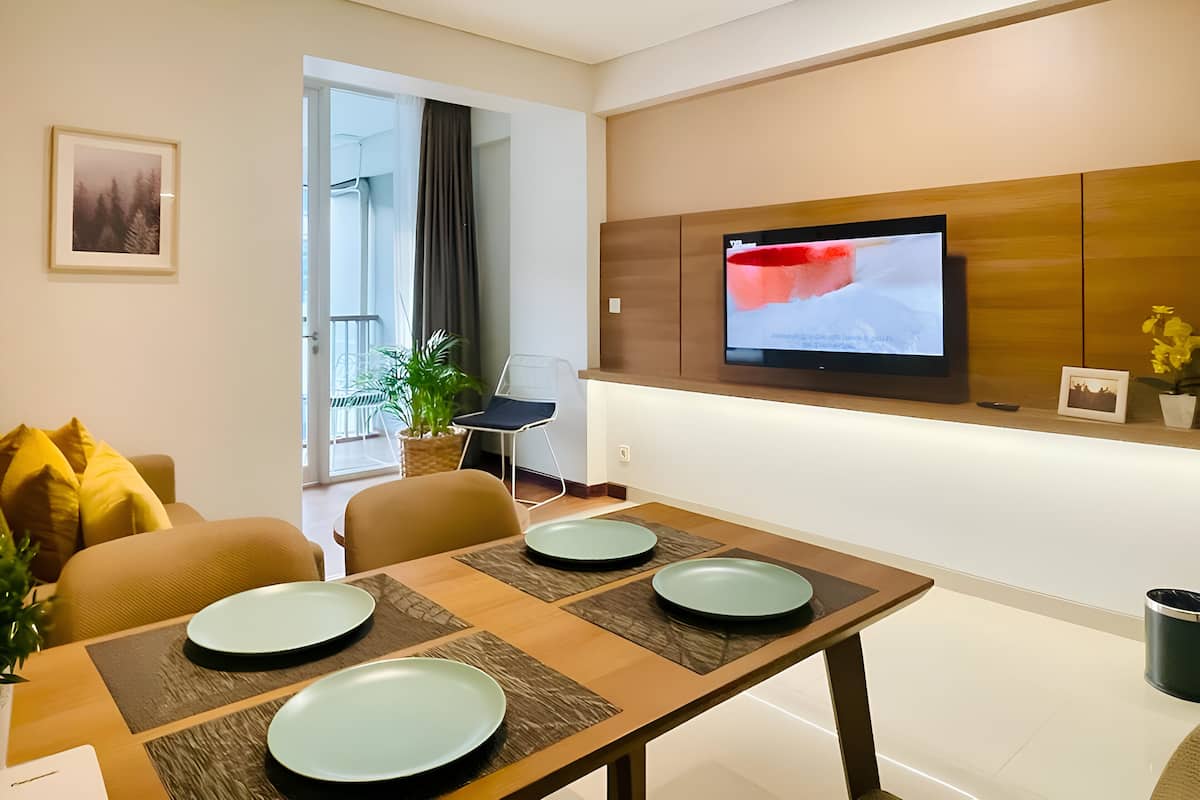 A modern dining area with a wooden table set for four, a television mounted on the wall, and a potted plant.