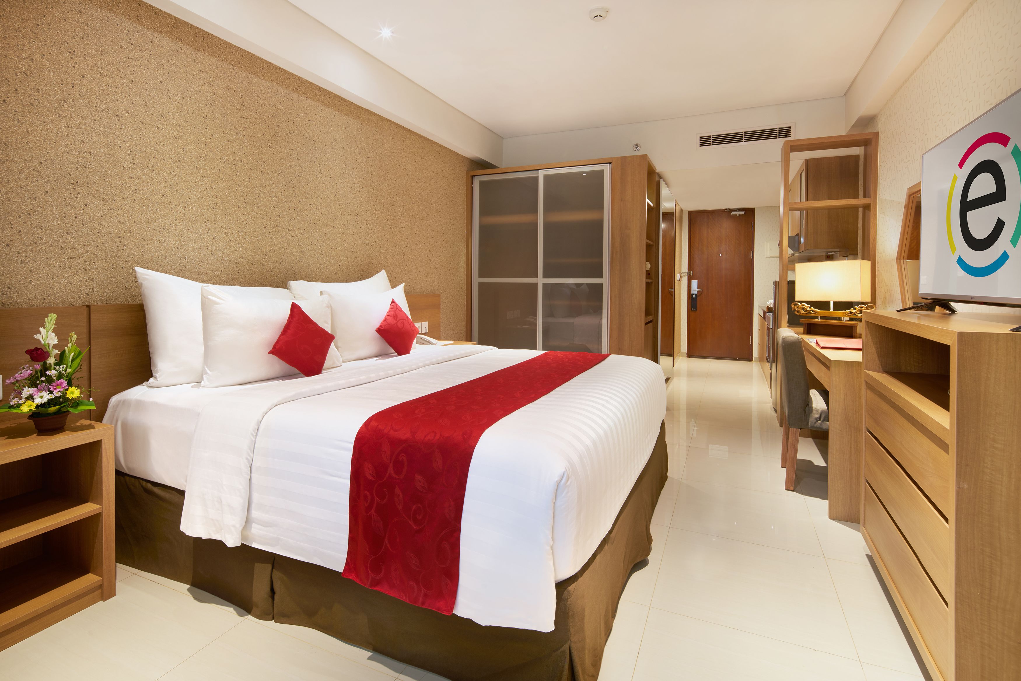 A hotel room with a large bed, wooden wardrobe, desk, and a TV.