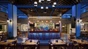 Un restaurant moderne doté d’un bar, de tables en bois et de luminaires suspendus.
