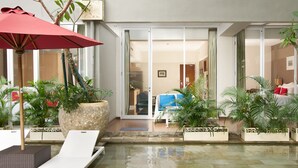 Un espace aménagé au bord de la piscine, avec des chaises longues, un parasol rouge et des plantes en pot.