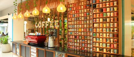 A coffee shop counter with a coffee machine, a display of colorful mugs, and hanging lights.