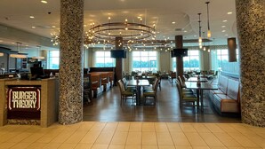 A spacious restaurant with high ceilings, stone pillars, and a central chandelier. Tables and booths are arranged for dining. - Holiday Inn Owensboro Riverfront by IHG (Owensboro)