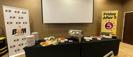 A conference room with a projector screen, a buffet table with various food items, and a banner reading 'Friday After 5'.