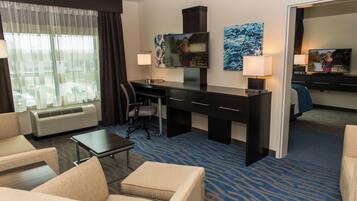 A hotel room with a desk, two chairs, a television, and a bed.