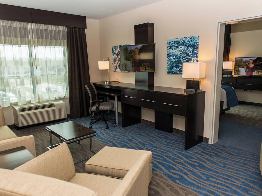 A hotel room with a desk, two chairs, a television, and a bed.