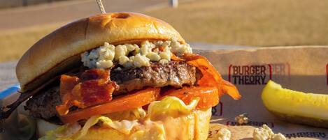Una hamburguesa con distintos ingredientes y una guarnición de pepinillos.