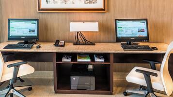 Un espacio de trabajo en un hotel con dos monitores, una lámpara de escritorio, un teléfono y una impresora HP sobre una encimera de mármol.