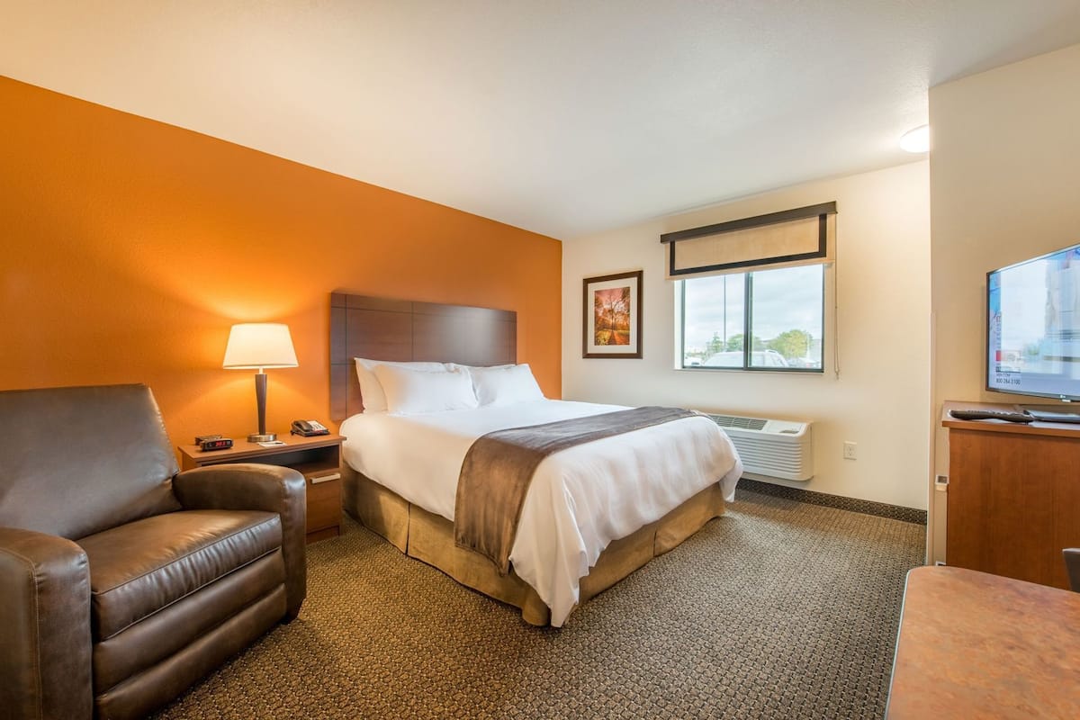 A hotel room with a bed, a chair, a desk, a lamp, a TV, and a window.