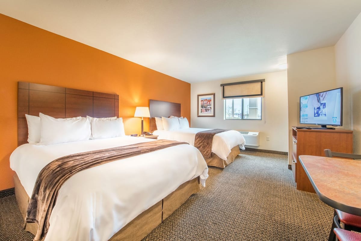 A hotel room with two beds, a desk, a television, and a window.