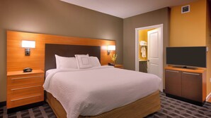 A hotel room with a large bed, wooden headboard, bedside lamps, a TV, a dresser, and a patterned carpet. - TownePlace Suites Missoula (Missoula)
