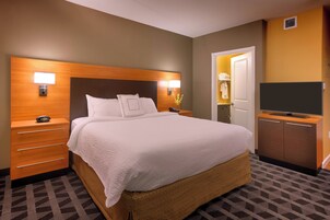 A hotel room with a large bed, wooden headboard, bedside lamps, a TV, a dresser, and a patterned carpet.