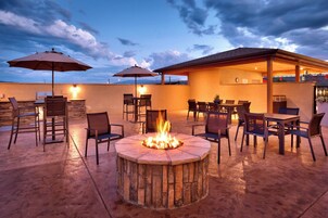 An outdoor patio with a stone fire pit, seating, and umbrellas.