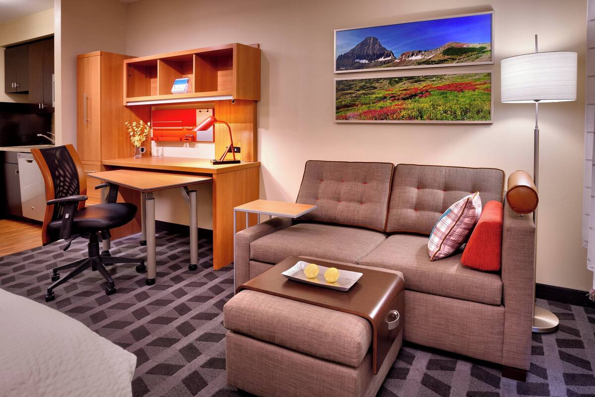 Habitación de hotel compacta con kitchenette, sofá, escritorio y comedor.