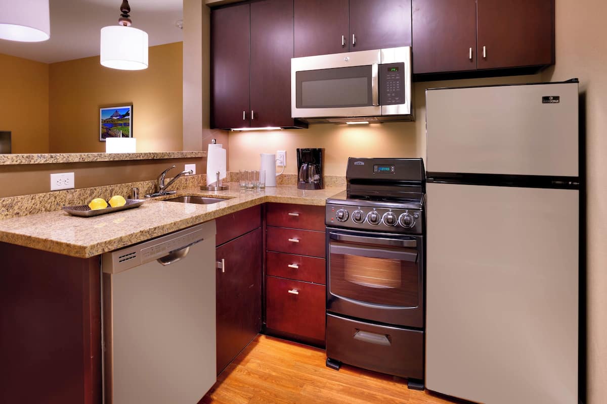 Una cocina con armarios de madera oscura, un microondas de acero inoxidable, un refrigerador y un horno empotrado.
