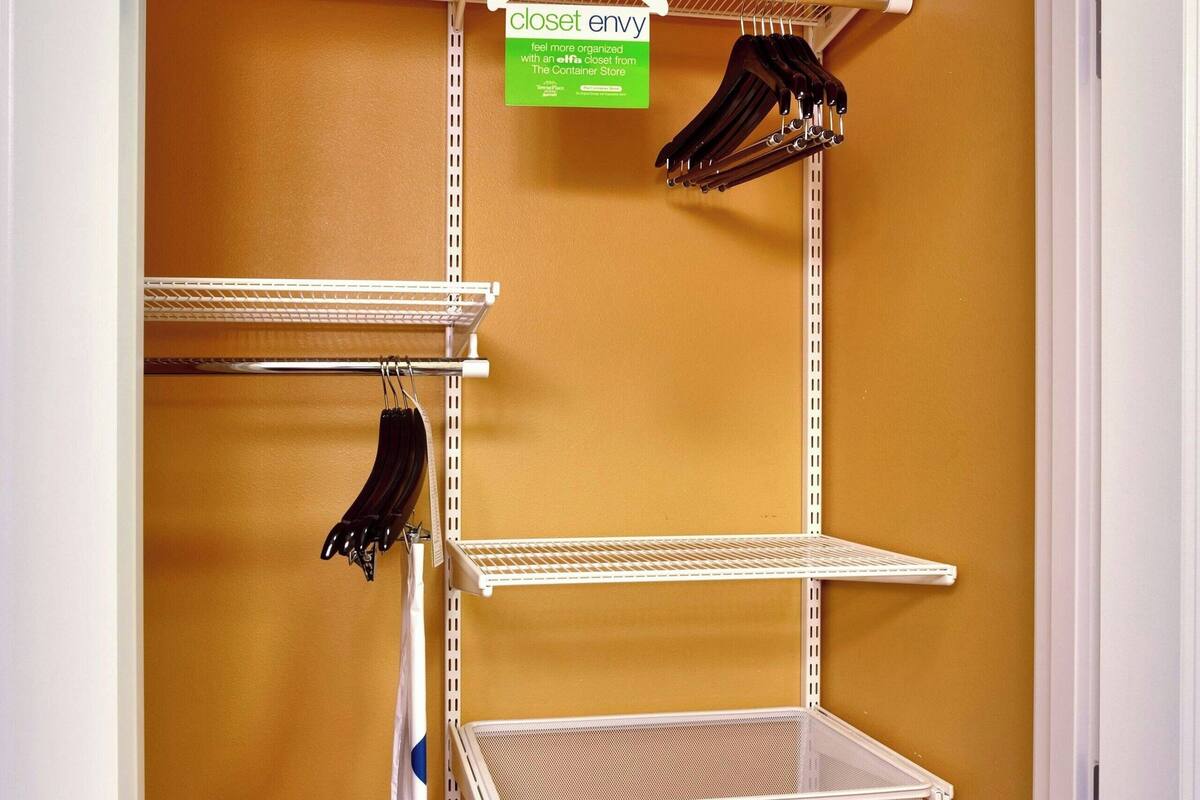 Un armario con repisas metálicas y perchas, un contenedor de almacenamiento blanco y un cartel que indica que pertenece a The Container Store.