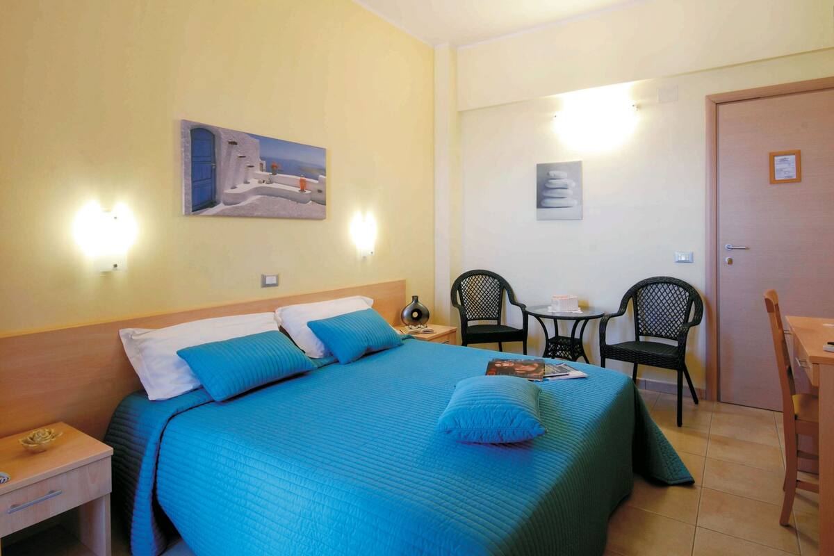 A hotel room with a bed, a desk, two chairs, and a small table.