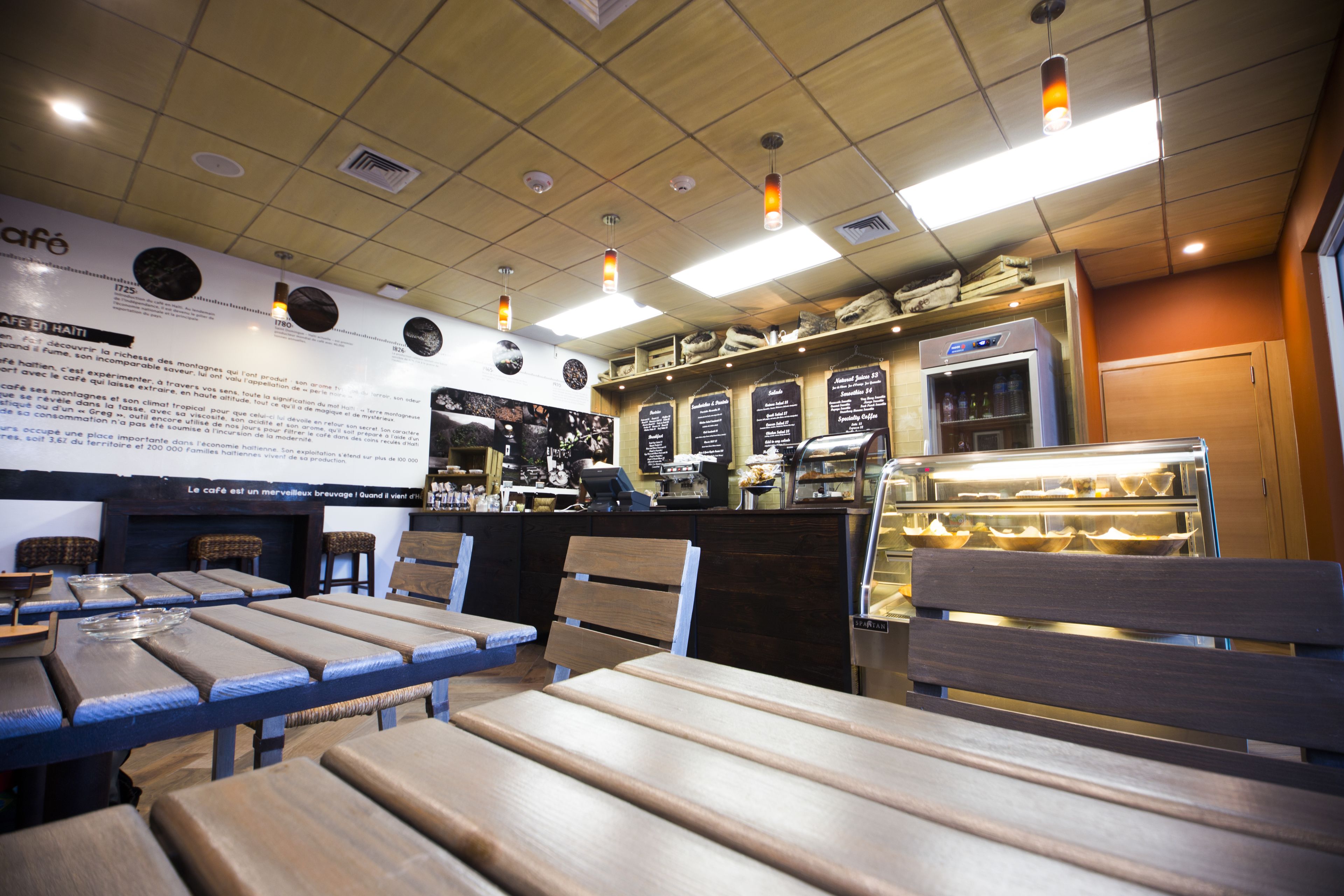A café interior with wooden tables and benches, a counter with a coffee machine, and a display case with baked goods.