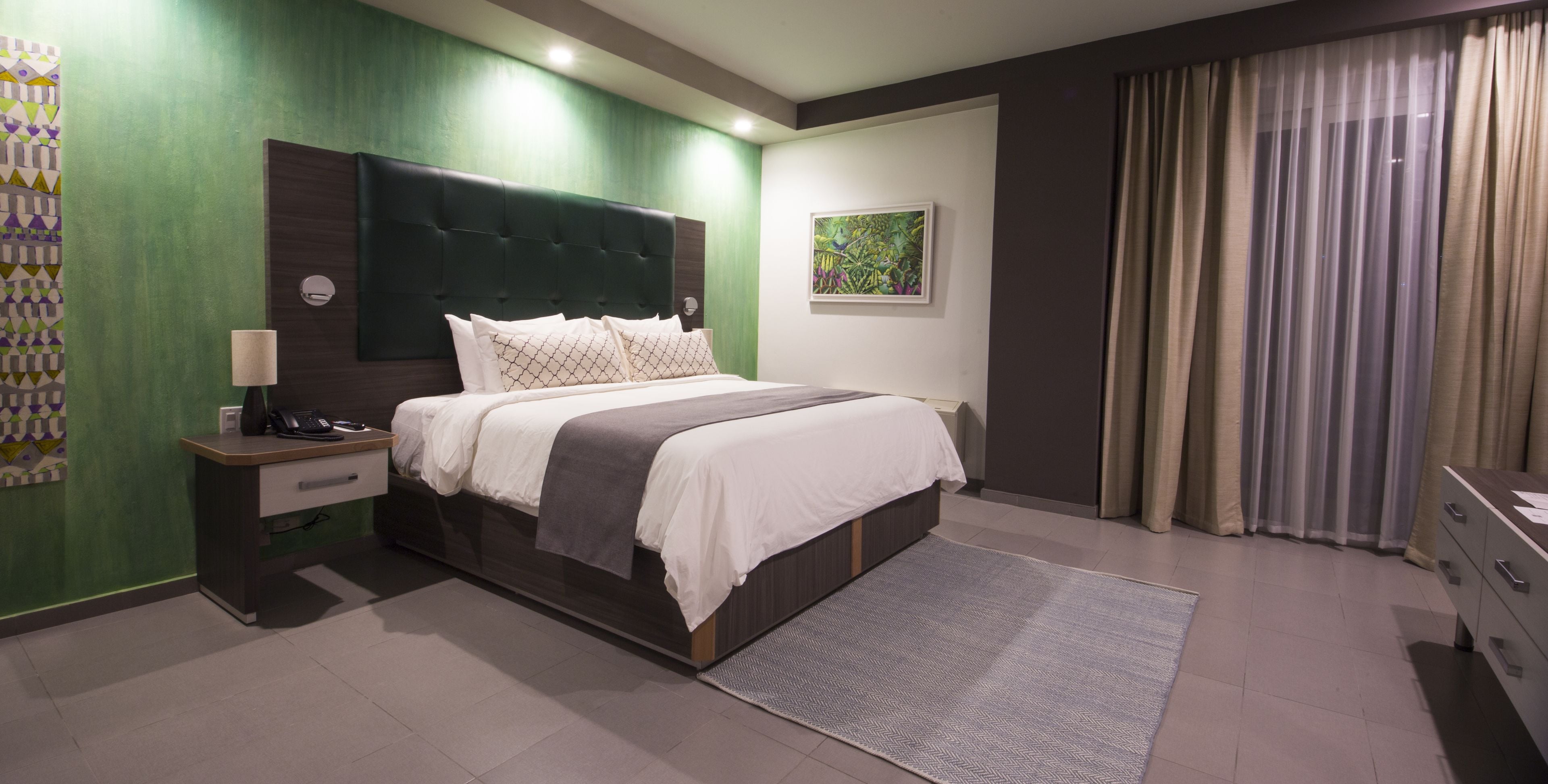 A modern bedroom with a large bed, a bedside table with a lamp, a desk, and a chair.
