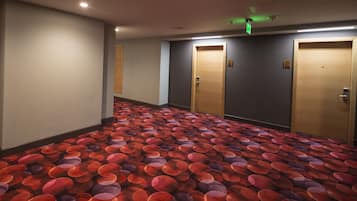 A hotel hallway with patterned carpet, wooden doors, and emergency exit signs.