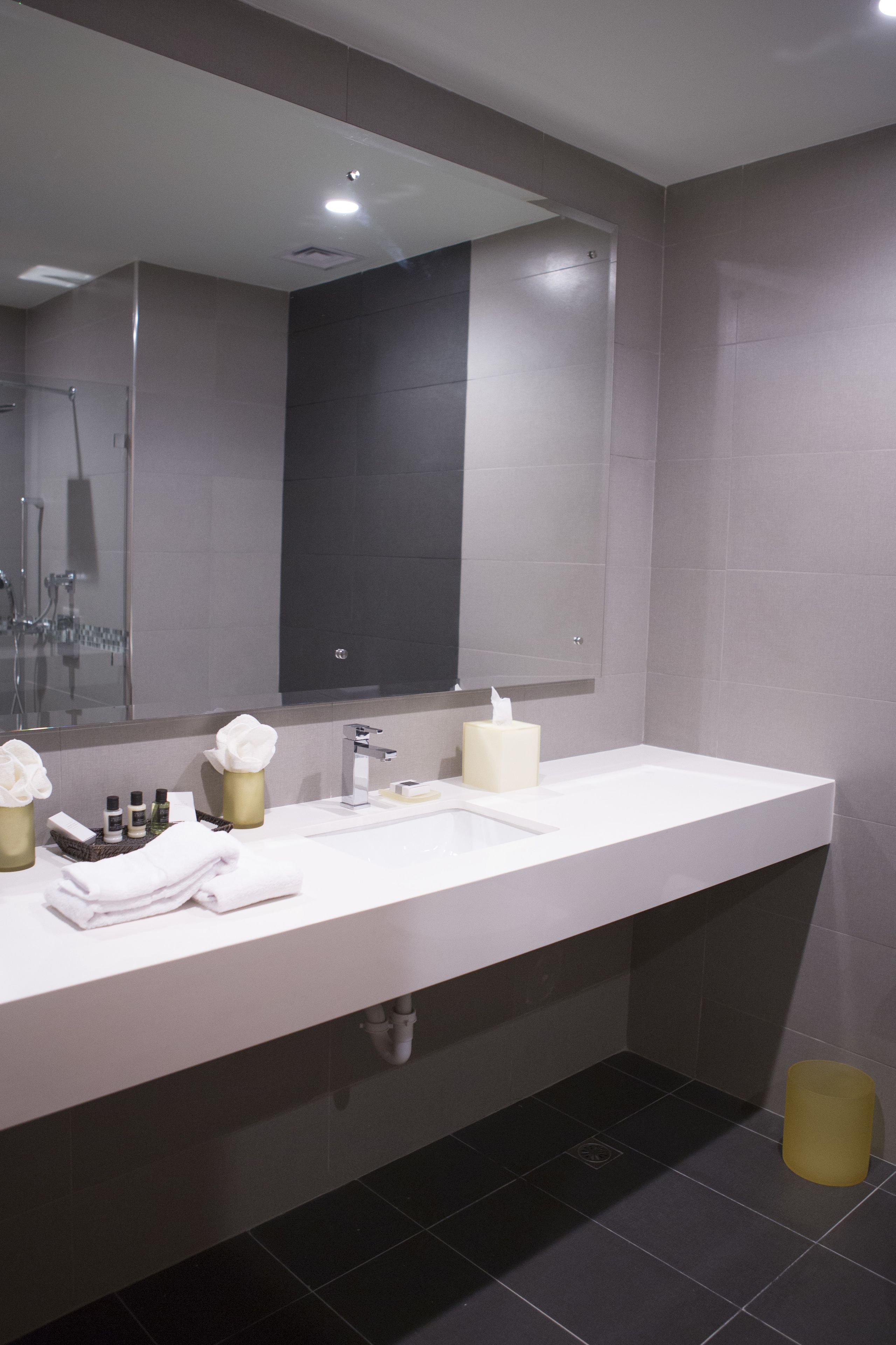 A modern bathroom with a large mirror, a white sink, and a shower area.