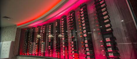 A wine cellar with rows of wine bottles, a white cushioned chair, and a curved ceiling with red lighting.