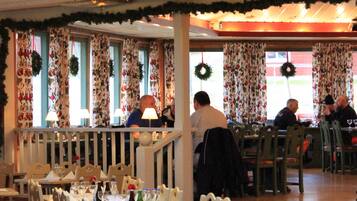 A restaurant with tables set for dining, a chandelier, and festive holiday decorations.
