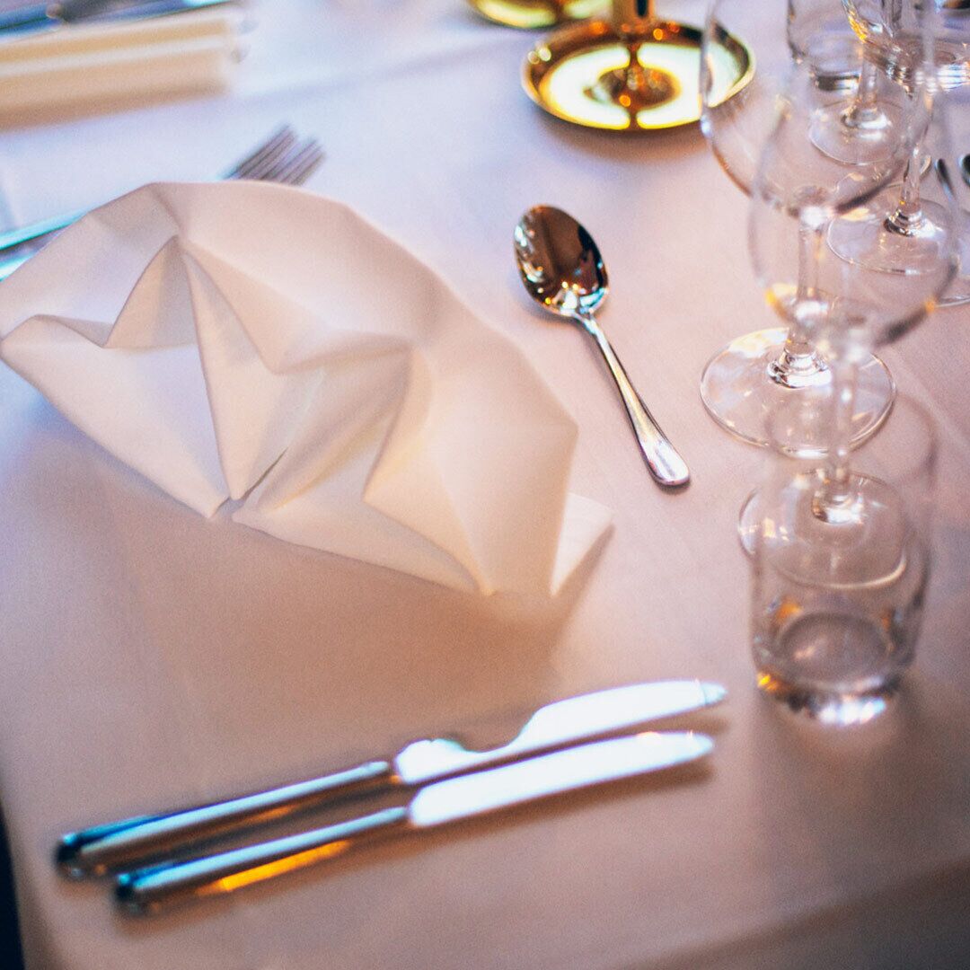 Una mesa dispuesta con un servilleta doblada, una cuchara, un cuchillo y copas de vino.