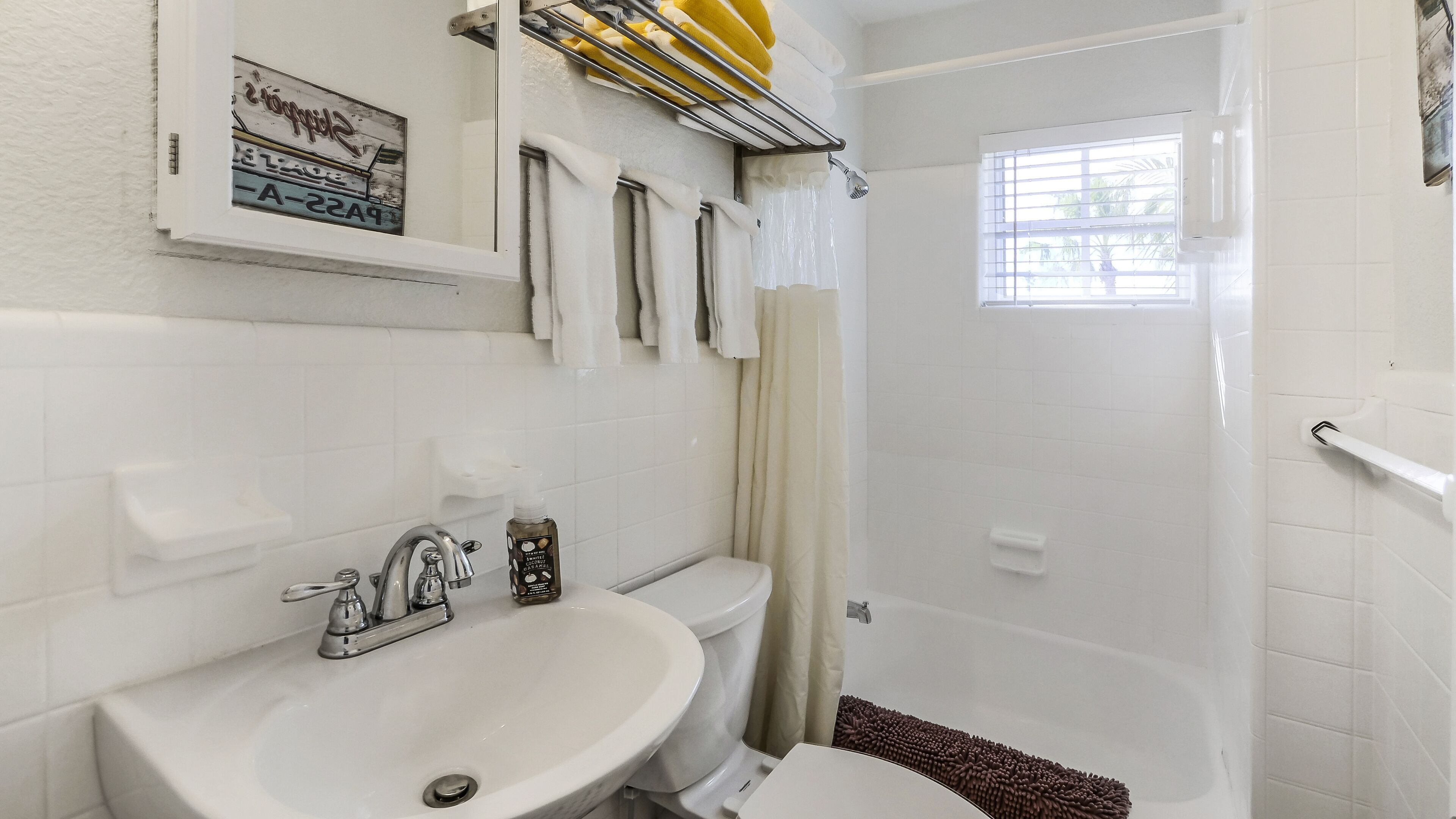 A bathroom with a sink, toilet, and shower. There are towels and a bottle of hand soap on the sink.