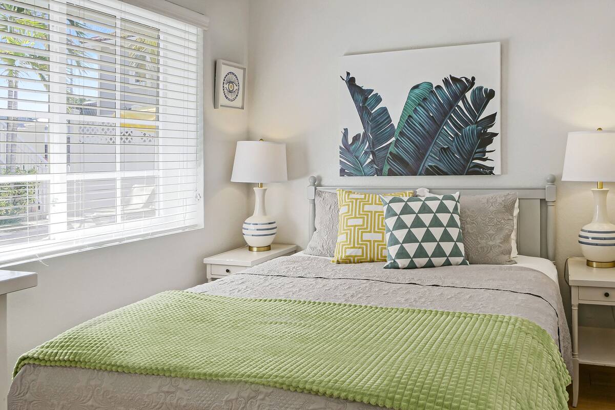 A neatly arranged bedroom with a bed, two bedside tables, a window with blinds, a wall-mounted artwork, and a radiator.