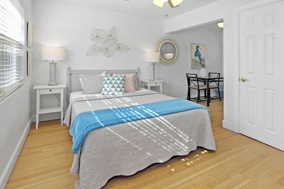 A bedroom with a bed, bedside tables, a desk, a chair, a mirror, and a door.
