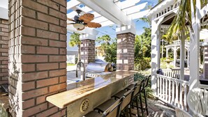 Un patio al aire libre con una parrilla, asientos y una estructura de pérgola blanca.