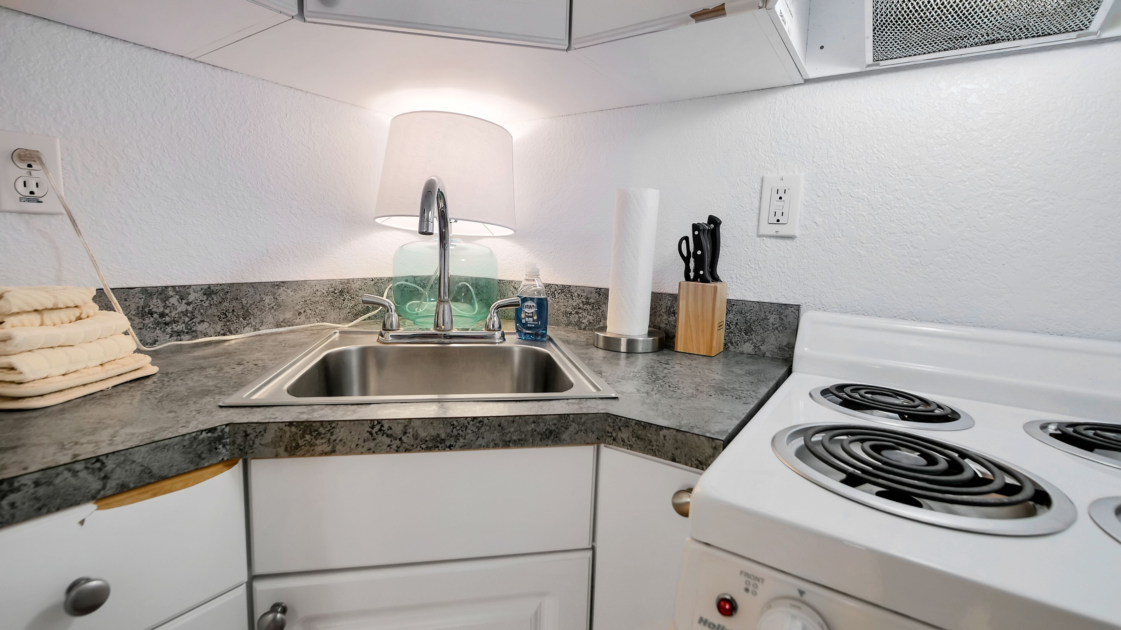 A kitchen with a stainless steel sink, a white stove, and a granite countertop.
