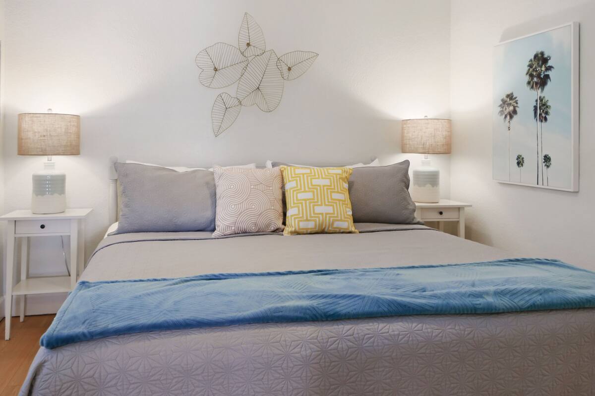 A bedroom with a bed, two bedside tables, a wall-mounted lamp, and a wall decoration.