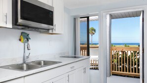 A kitchen with a microwave, double sink, and a view of the beach through an open door. - Sabal Palms Inn (St. Pete Beach)