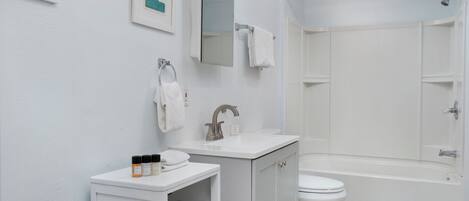 A modern bathroom with a white sink, vanity, and toilet. There is a shower area with a glass door and a blue mat.