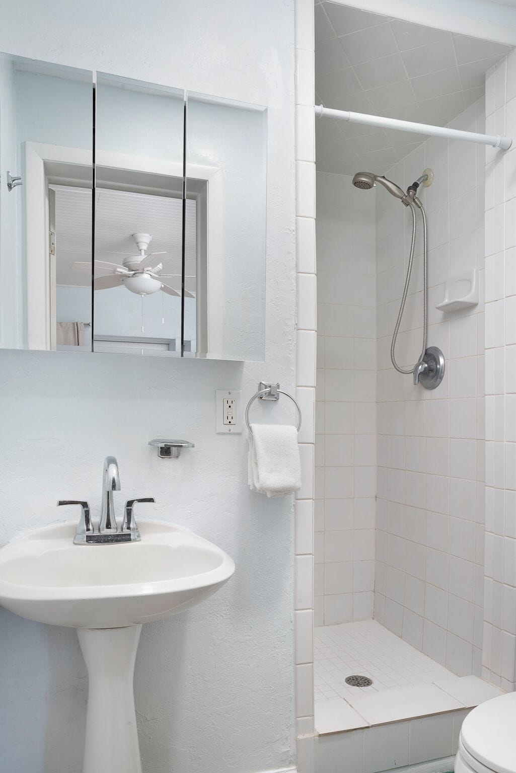 A bathroom with a white sink, a mirror, a ceiling fan, and a shower area.