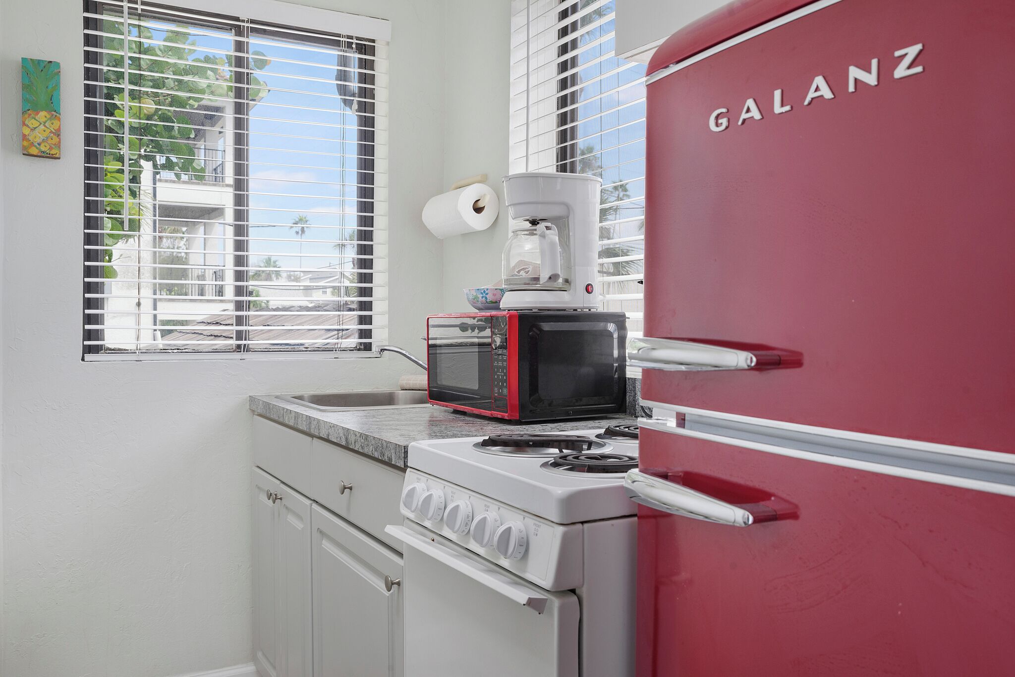 A compact kitchen with a white stove, a red Galanz refrigerator, a microwave, and a coffee maker.