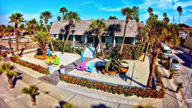 A building with a sloped roof, surrounded by palm trees and a landscaped area with outdoor seating. - Sabal Palms Inn (St. Pete Beach)
