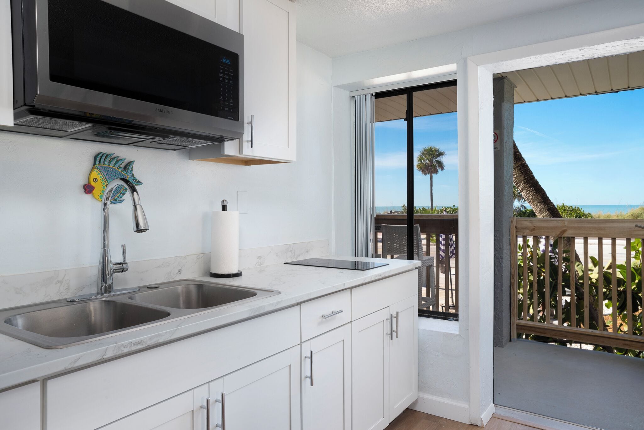 A kitchen with a large stainless steel sink, a microwave, and a decorative fish.