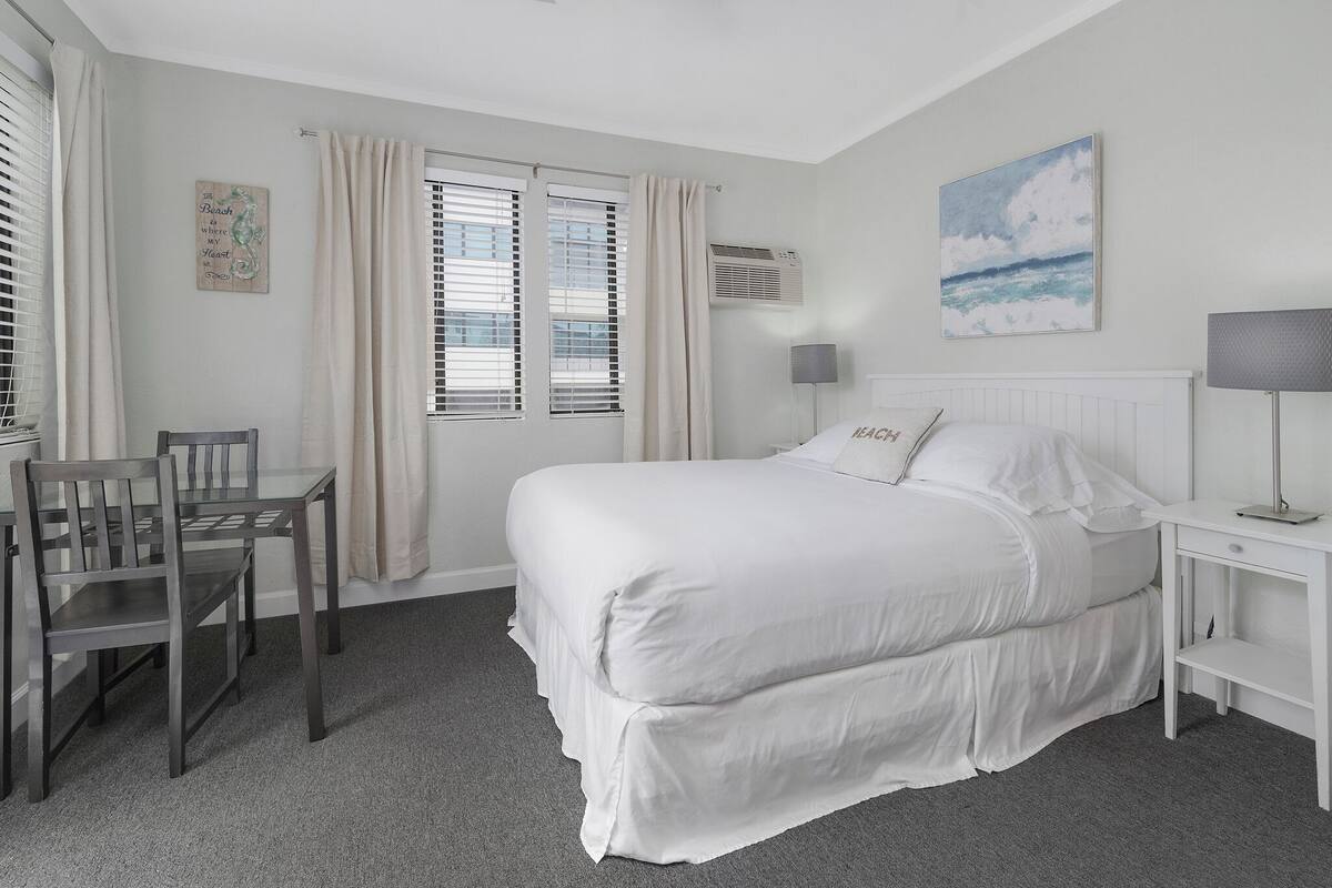 Un dormitorio con una cama grande, un escritorio, una silla y una ventana con cortinas.