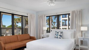 A hotel room with a bed, a sofa, and a view of palm trees and a balcony. - Sabal Palms Inn (St. Pete Beach)