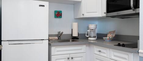 A kitchen with white cabinets, a refrigerator, a microwave, and a coffee maker.
