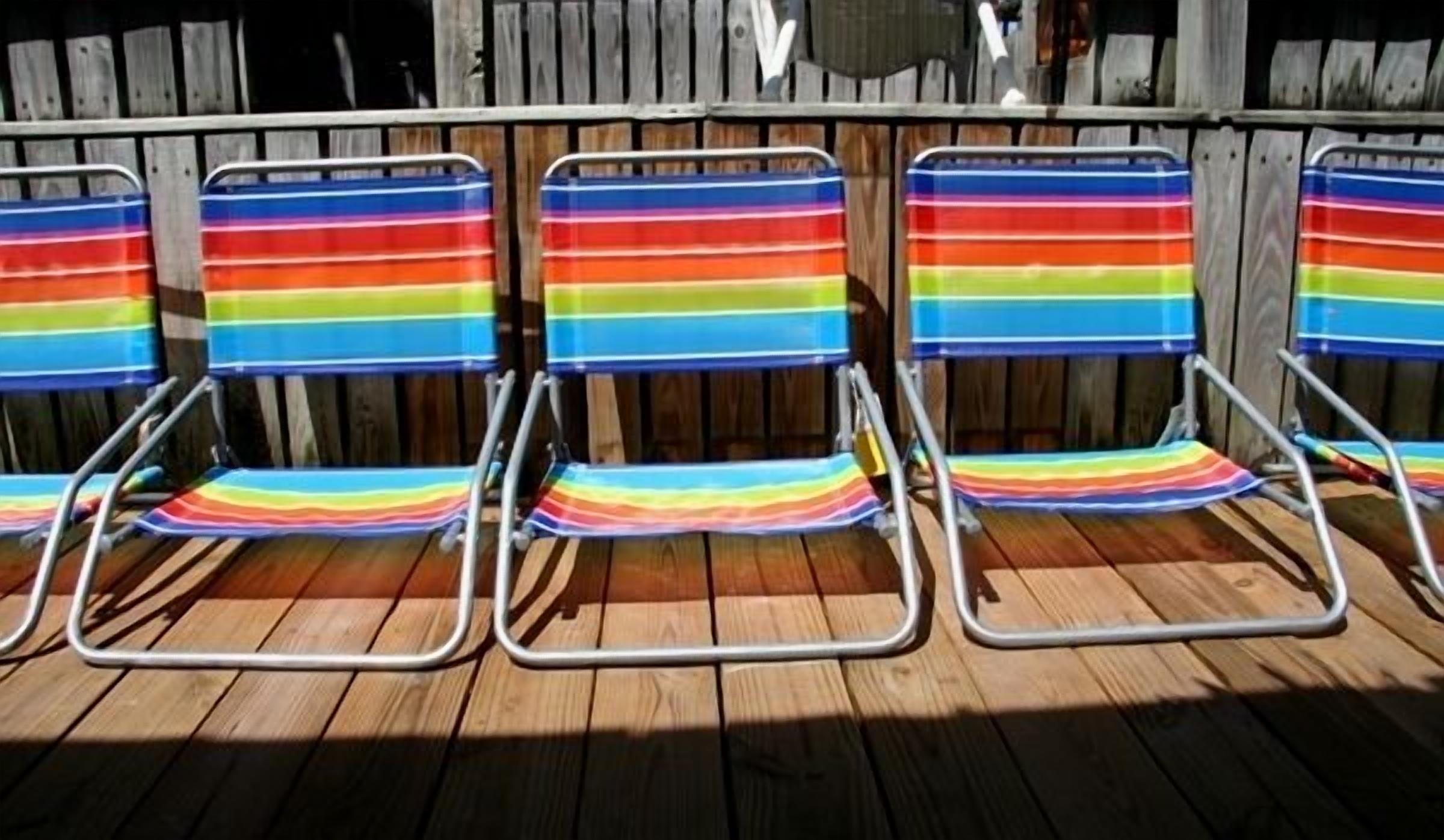 Four beach chairs with colorful striped cushions, arranged in a row on a wooden deck.