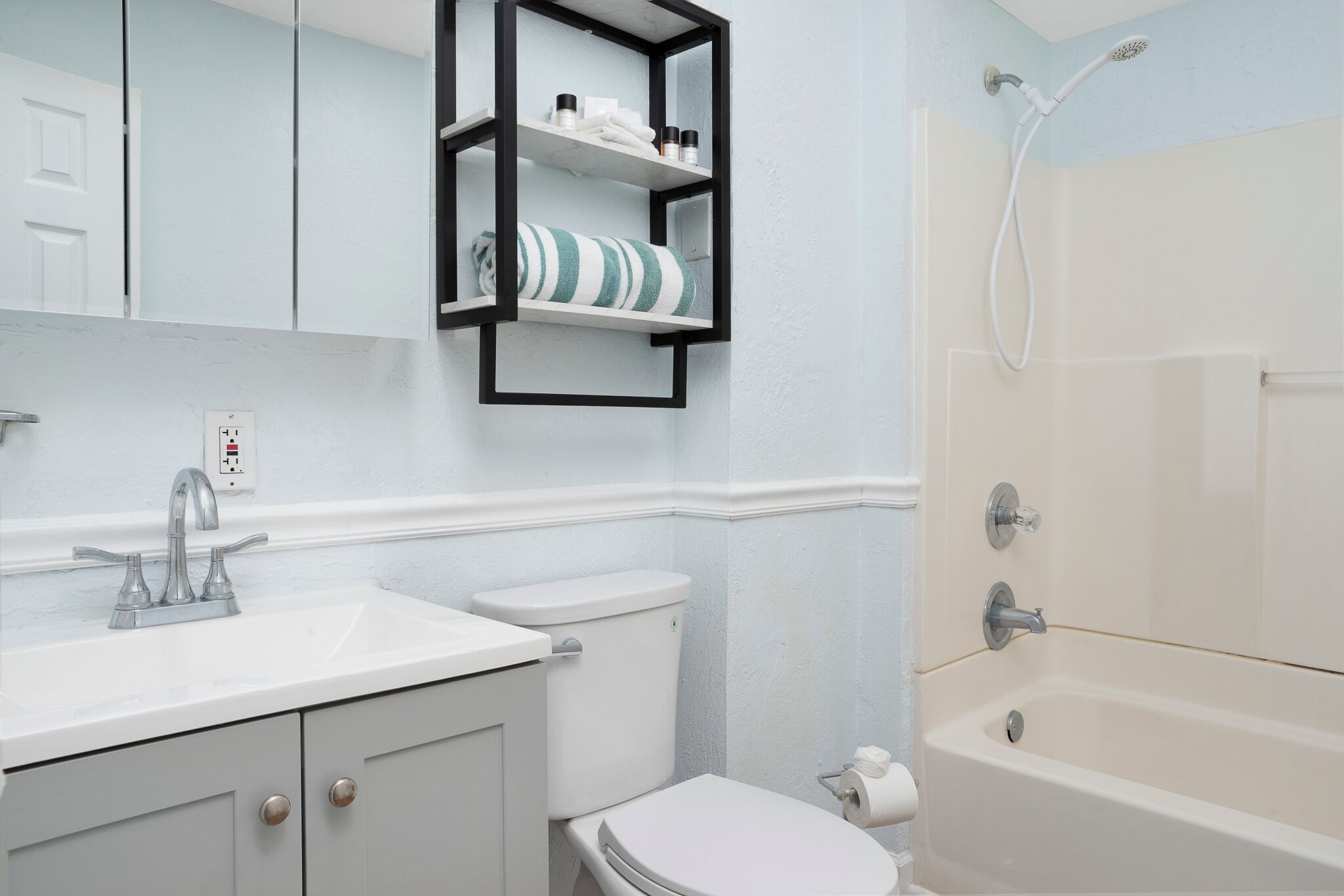 A bathroom with a white sink, a toilet, a bathtub, and a shelf with toiletries.