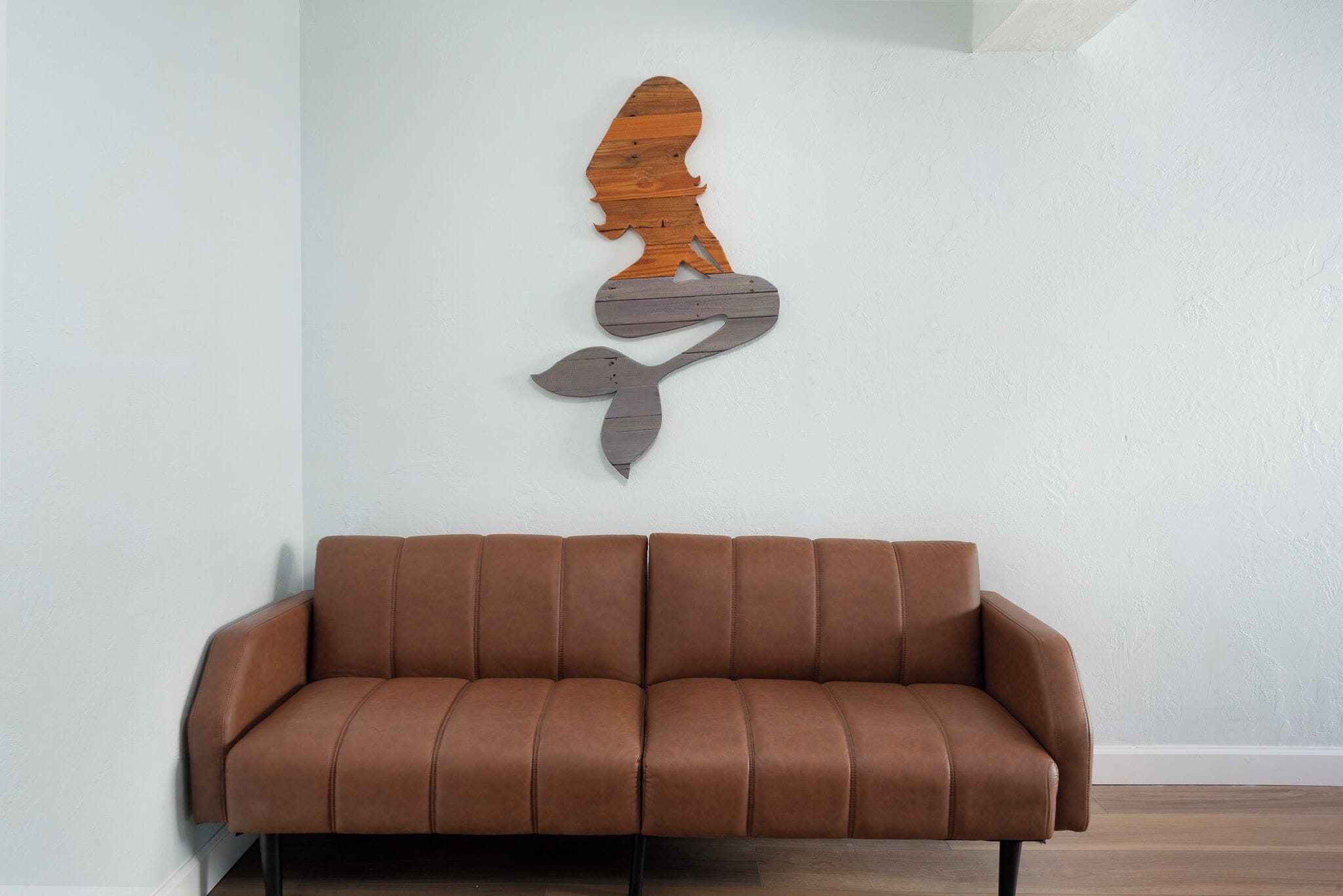 A brown leather sofa against a white wall with a wooden silhouette artwork.