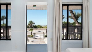 A room with a bed, a window with a view of a beach and palm trees, and a door leading outside. - Sabal Palms Inn (St. Pete Beach)